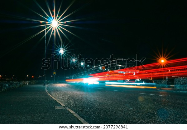 Night scene with car trail on a small narrow\
road. City lights illuminated with light burst. Late traffic\
concept. Transport at dark\
time.