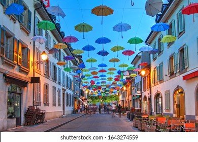 Night scene in Carouge, Geneva, Switzerland along Rue Saint Joseph covered by colorful umbrellas.