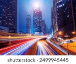 A night scene of a Hong Kong street with tall buildings and brightly lit windows. Light trails from cars moving along the street create a colorful and dynamic scene.