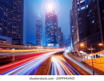 A night scene of a Hong Kong street with tall buildings and brightly lit windows. Light trails from cars moving along the street create a colorful and dynamic scene. - Powered by Shutterstock