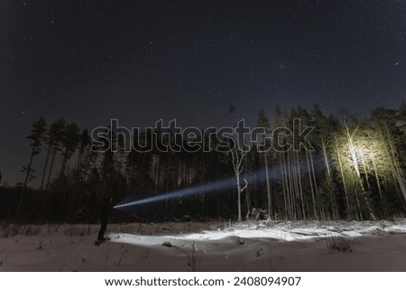 Night scene, a man with a flashlight in the forest in winter. Starry sky. High quality photo