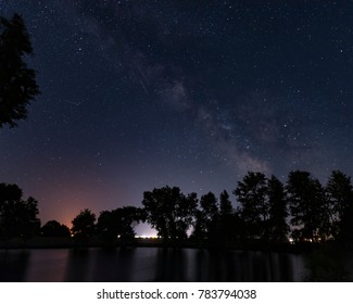 Night scene with the Milky Way above the Dark Waters of a Pond with Trees in Sihouette - Shutterstock ID 783794038