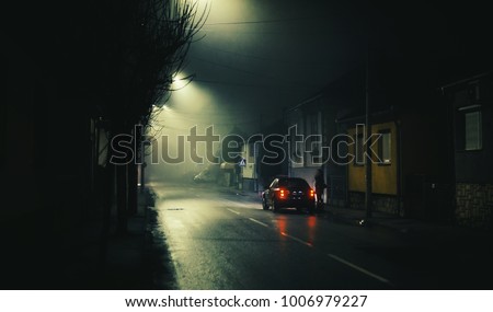 Night scene on foggy street of a small town, lonely woman and one car. 