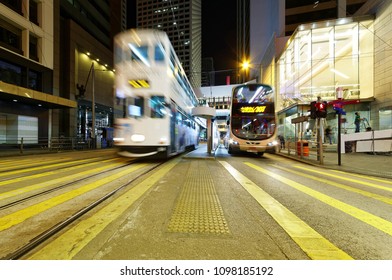 Night Scenery Of Downtown Hong Kong With A Double-decker Tram Moving Fast On The Tracks Amid Highrise Office Towers & A Bus Traveling Under A Pedestrian Footbridge Near The Landmark Square In Hongkong