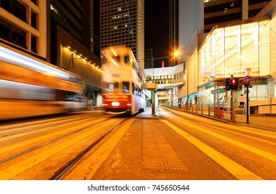 Night Scenery Of Downtown Hong Kong With A Streetcar Moving Fast On The Tracks Among High-rise Office Towers ~A Trolley Bus Traveling Under A Pedestrian Footbridge Near The Landmark Square In Hongkong