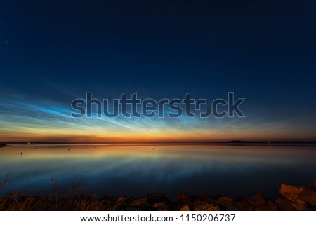 Night shining clouds (noctilucent clouds) over lake in Sweden, with kinnekulle in the background