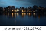 Night shot of houses in Dutch village on riverbank. Lights reflecting on water surface