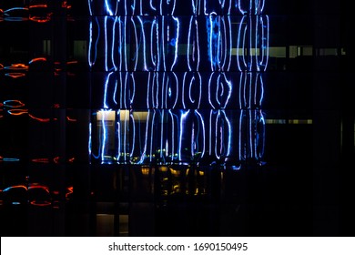 A Night Shot Showcasing The Colorful Neon Lights Reflecting Off A High Rise Office Buildings Glass Facade.  