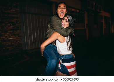 Night Shot Young Woman Lifting Her Best Friend Laughing. Female Friends Hanging Out And Having Fun.