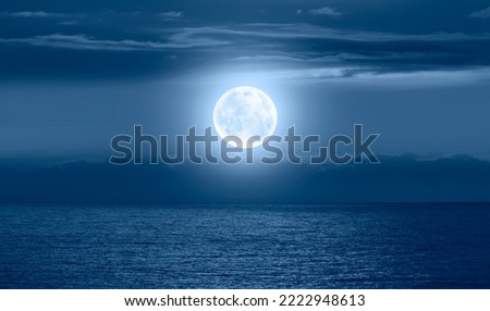 Night sky with moon in the dark clouds and darkblue sea in the foreground 