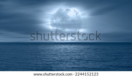 Night sky with moon in the dark clouds and darkblue sea in the foreground 