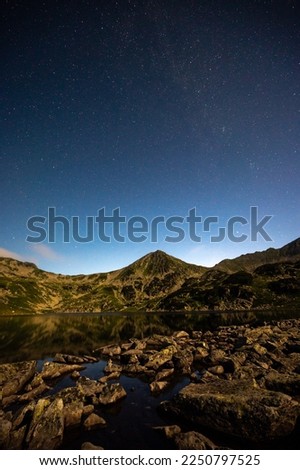 night sky with stars and hills of mountains in romanian mountain range retezat in carpathians in transylvania with the lake
