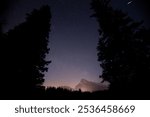 Night sky with stars, mountains in the distance, tree silhouette at midnight