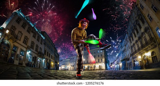 Night Street Circus Performance Whit Clown, Juggler. Festival City Background. Fireworks And Celebration Atmosphere.