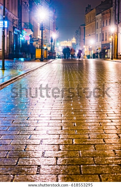 Night street in the Krakow, Poland.\
Colorful night illumination reflecting in the wet stone pavement of\
the old town. Beautiful background\
photo.