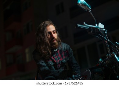 Night Street Portrait Of Young Guy With Long Hair On A Black Motorcycle