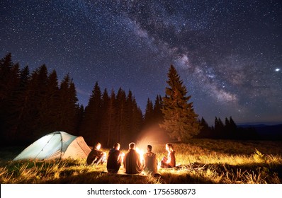 Nachts Sommercampingplatz in den Bergen, Fichtenwald auf Hintergrund, Himmel mit Sternen und Milchweg. Zurück-Gruppe von fünf Touristen, die zusammen um das Lagerfeuer ruhen und frische Luft in der Nähe des Zeltes genießen.