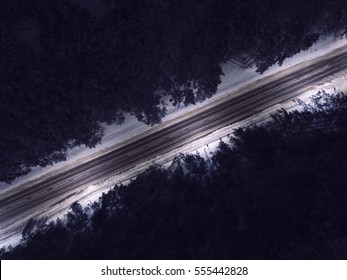 Night Time Aerial Top Down View Of A Snowy Road Surrounded Pine Tree Forest In Winter Season.