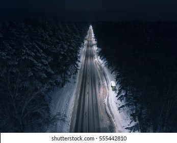 Night time aerial view of a snowy road surrounded pine tree forest in winter season.