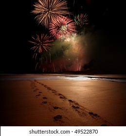 Night time celebration at the beach with fireworks and footprints in the sand.