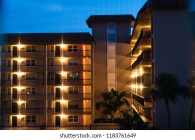 Night Time Establishing Shot Looking At Generic Apartment Condo Building Balcony Entrances On Multiple Floors. Porch Lights Illunimate Dark Setting