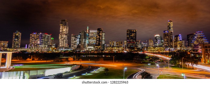 Night time exposure of the Austin Texas skyline with buildings illuminated and light reflecting off of the clouds in an overcast sky and streaks from cars crossing the Colorado river and side streets