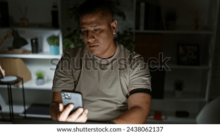 Night time hustle, young, serious latin man, a hard-working business professional, immersed in texting on his smartphone at the office desk.