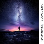 Night time long exposure landscape photography. A man standing in a high place looking up in wonder to the Milky Way galaxy, photo composite.