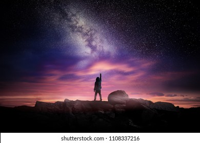 Night time long exposure landscape photography. A man standing in a high place reaching up in wonder to the Milky Way galaxy, photo composite. - Shutterstock ID 1108337216