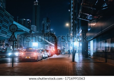 Night urban street in Dubai downtown with taxi cars, high rise buildings and evening illumination, toned
