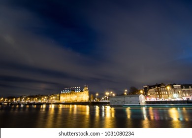 Night View Of An Amsterdam Canal From The Central Station With A Boat Leaving Its Luminous Wake