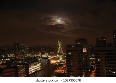 Night view of the city skyline with bridge and buildings under cloudy and full moon in the city of São Paulo. The gigantic city, famous for its cultural and business vocation.