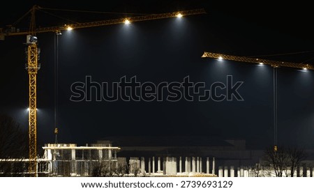 Night view of a construction site with two tall cranes illuminating a concrete structure. Light fog, cold atmosphere, urban industrial scene, and winter night concept.