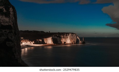 
night view of the iconic Etretat rock formations in Normandy, France. Illuminated by moonlight, with shimmering stars and gentle waves reflecting the serene beauty of the coastline, taken from a parc - Powered by Shutterstock