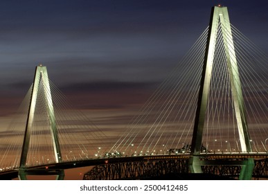 Night view of the illuminated Arthur Ravenel Jr. Bridge in Charleston, SC, against a twilight sky, showcasing its iconic cable-stayed design and modern architecture. - Powered by Shutterstock