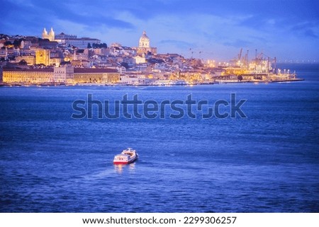 Night view of Lisbon over Tagus river from Almada with ferry and tourist boat in evening twilight. Lisbon, Portugal