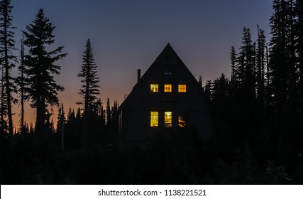 Night View Of A Mountain Cabin In The Woods; Windows Brightly Lit