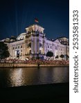 Night view of the Reichstag building in Berlin, Germany, with a crowd gathered by the river and illuminated by lights.