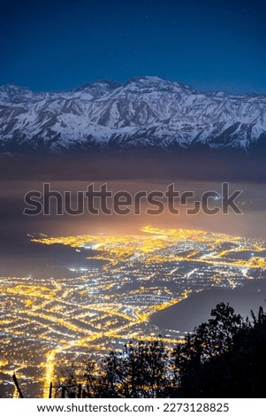 Night view of Santiago de Chile with snowy mountains in the background captured in a photograph.