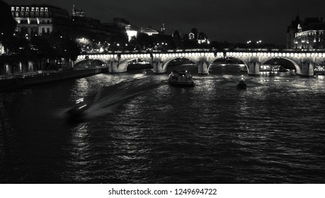 Night View Of Seine River With Pont Neuf Bridge, Touristic Ship And Two Police Boats Coming. Paris, France. Black And White Photo.