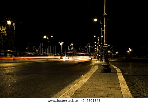 Night view of a street in San Giovanni\
in Rome, with the lights of cars and street\
lamps.