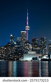 Night view of Toronto skyline with CN Tower illuminated in pink, reflecting on Lake Ontario.