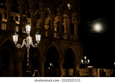 A night view of Venice with a brightly lit vintage street lamp against the backdrop of the famous architecture of the Doge's Palace. The moonlight enhances the mystical atmosphere of the city,  - Powered by Shutterstock