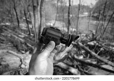 Night Vision Device In Hand Against The Backdrop Of A Forest, Black And White Photo.