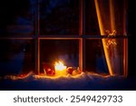 Night window of a wooden house in a winter forest. Christmas candles and decorations are visible through the window