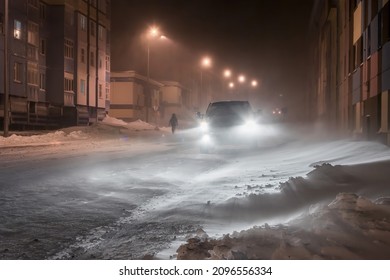 Night winter view of a snow-covered street in a northern city in the Arctic. The car is driving on a snowy road. Cold winter weather. Bad visibility. Harsh polar climate. Anadyr, Chukotka, Russia.