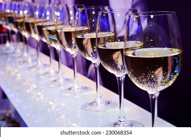 Nightclub wine glasses with white wine lit by festive lights on dark-purple background