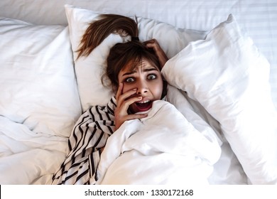 Nightmare and Insomnia.  Horror dream. Wake up. Emotions. Girl in pajama is looking at camera and screaming while lying in a bed at home, top view