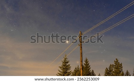 Nightphotography with long exposure capturing an old powerline and night sky with stars and the moon