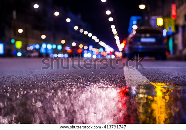 Nights lights of the big city, the main\
city street with parked car. Close up view from the level of the\
dividing line, in blue tones, focus on the\
asphalt